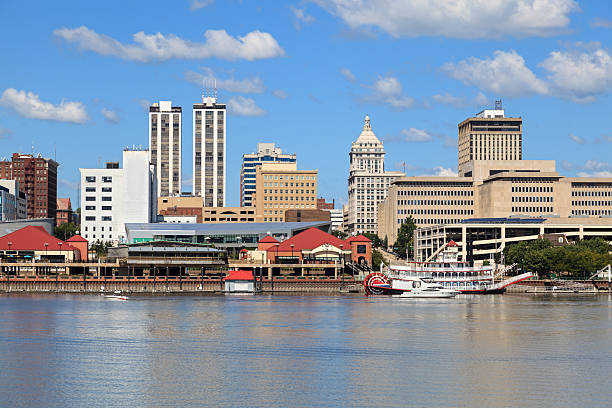 View of Peoria's river front showing downtown buildings, bridge, the Illinois river, blue sky in background.